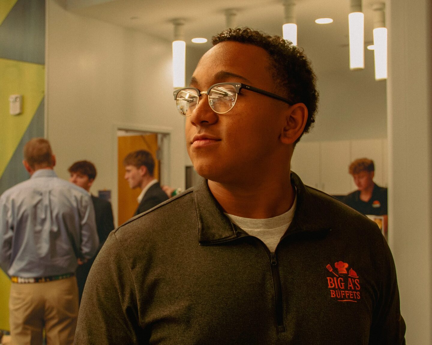 Adrian wearing glasses and a black Big A's Buffets polo at an indoor event.
