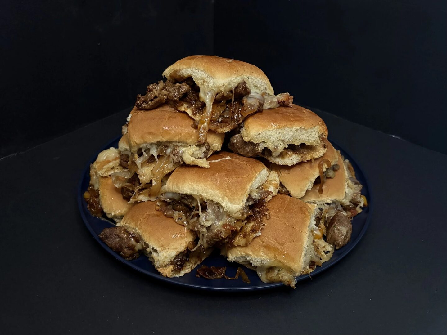 Philly's Nephews steak sliders piled on a platter with melted cheese and onions.