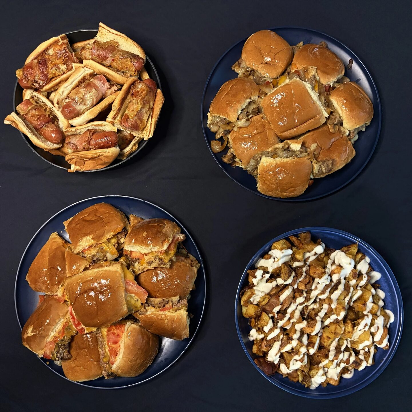 An overhead spread of bacon-wrapped hot dogs, steak sliders, cheeseburger sliders, and loaded potatoes.
