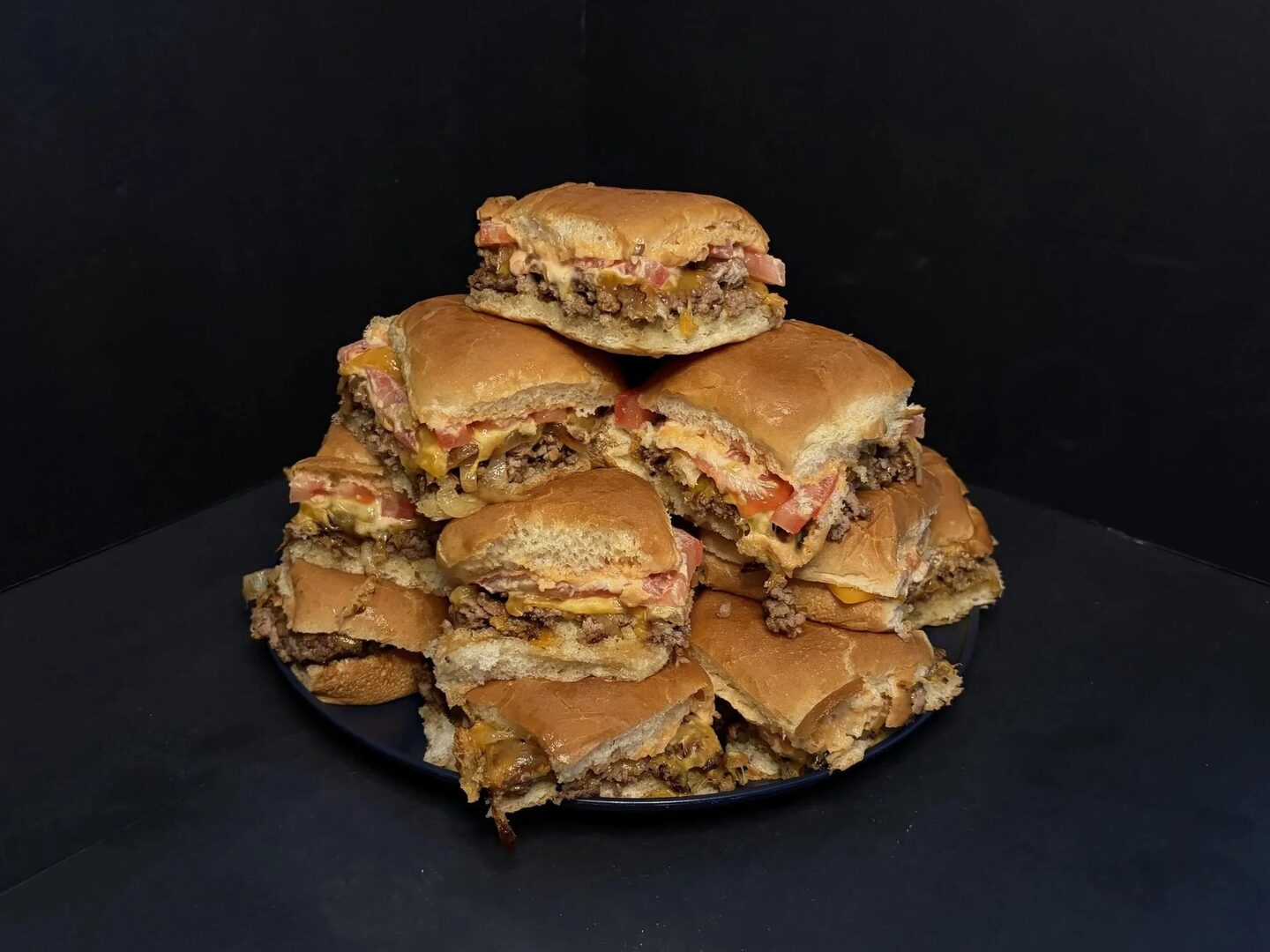 Smashlet Sliders stacked on a platter, with beef, melted cheese, tomatoes, and smash sauce.